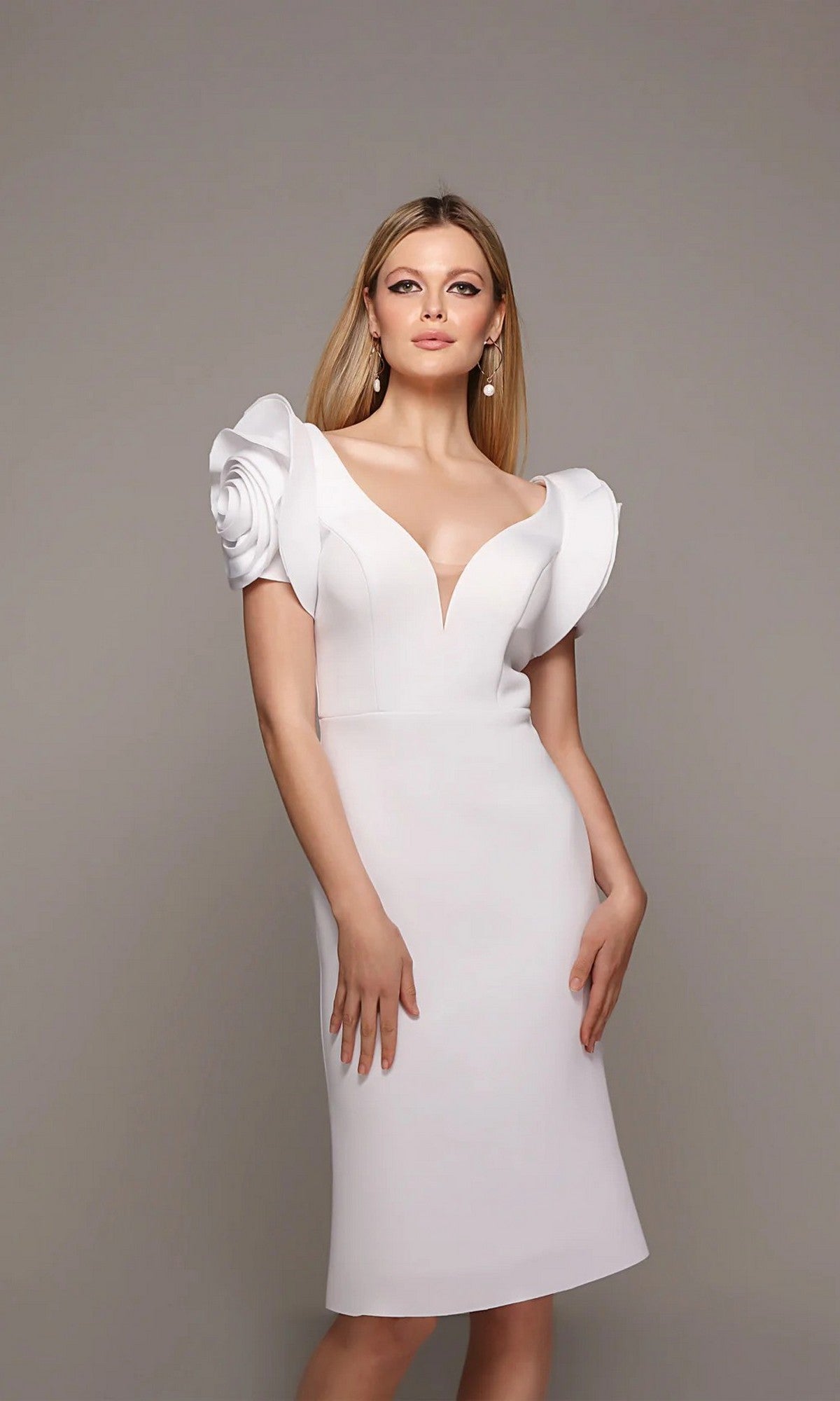 A woman models the Alyce 70024 Knee Length White Party Dress in Diamond White, featuring 3D floral sleeves, a deep V neckline, and structured ruffle detailing for a chic, modern look against a plain gray background.